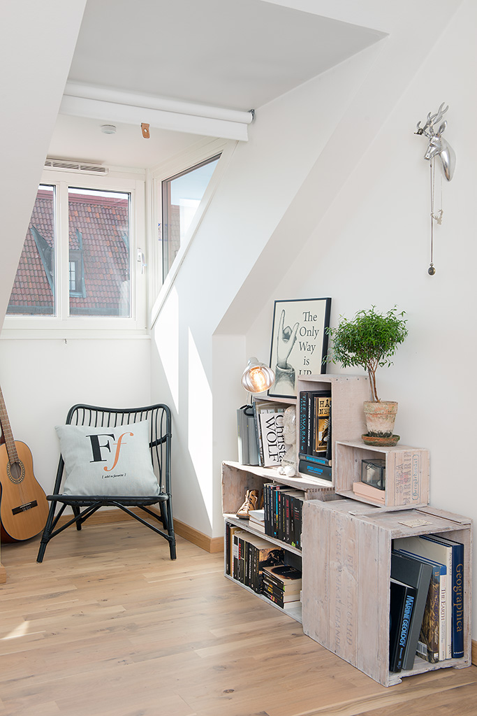Кресло с подушкой в углу, гитара и книжный шкаф на чердаке в небольшой квартире в Швеции