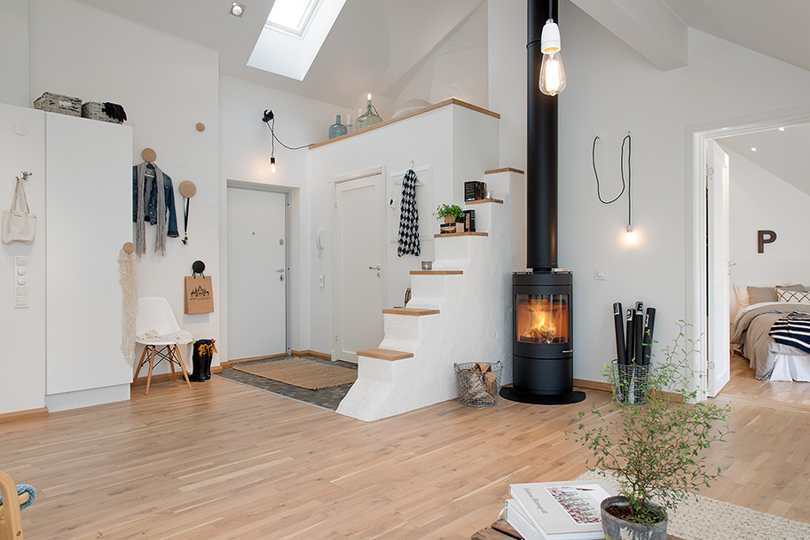 Чёрный камин с интерьере светлой гостиной на чердаке небольшой квартиры в Швеции