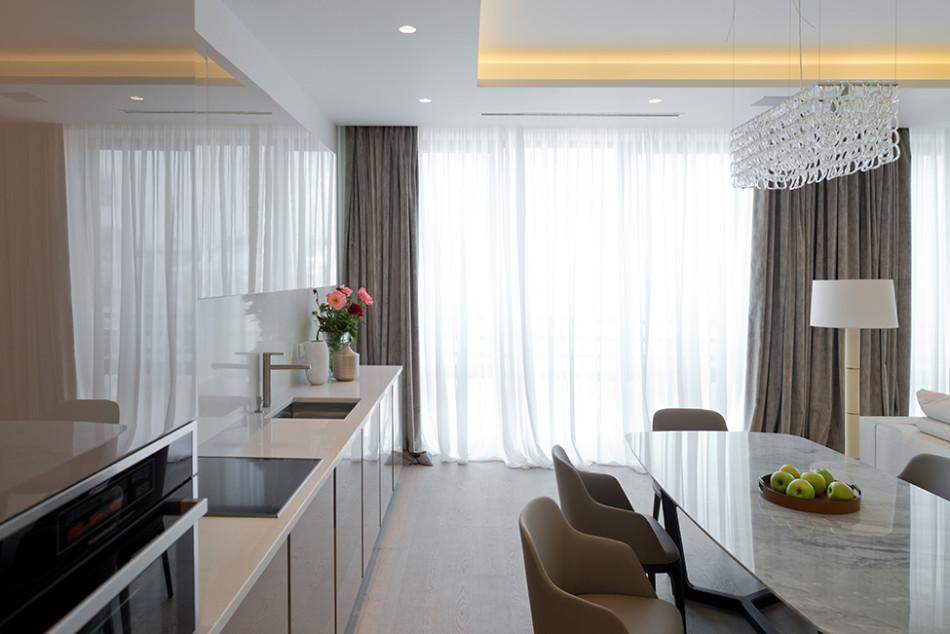Светлая кухонная мебель, шторы в пастельных тонах и потолочная подсветка в роскошной столовой