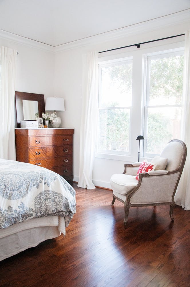 Элегантный интерьер белой спальни с деревянным комодом и креслом в классическом стиле